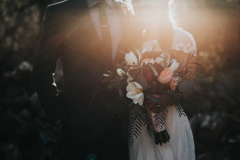 Couple in flowing wedding attire on a rocky Pacific coast beach at sunset